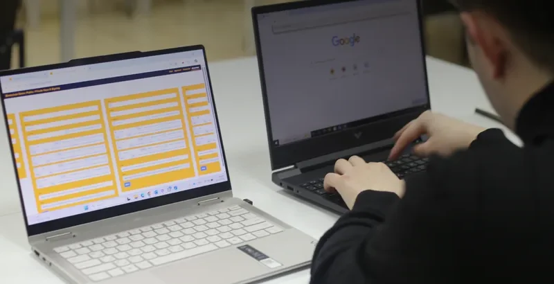 A law student at two laptops in a university classroom, working with a LegalTech Lab blockchain teaching simulator.