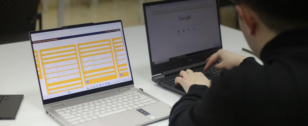 A law student at two laptops in a university classroom, working with a LegalTech Lab blockchain teaching simulator.