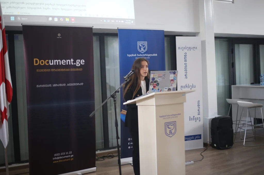 A student presenting a contract-automation capstone project at a lectern, with Document.ge and Sulkhan-Saba Orbeliani University banners behind her and a draft document on the projector screen.