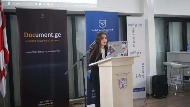 A student presenting a contract-automation capstone project at a lectern, with Document.ge and Sulkhan-Saba Orbeliani University banners behind her and a draft document on the projector screen.